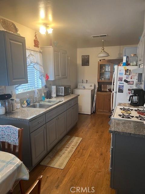 kitchen with a sink, light wood-type flooring, stainless steel microwave, washer / clothes dryer, and freestanding refrigerator