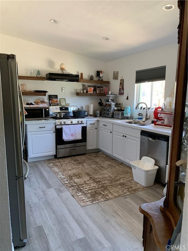 kitchen with stainless steel appliances, light wood-style floors, extractor fan, white cabinets, and a sink