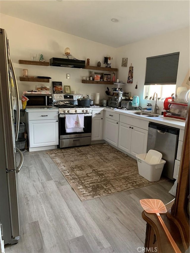 kitchen featuring light wood-style floors, appliances with stainless steel finishes, white cabinets, range hood, and a sink