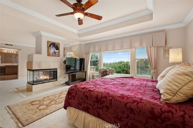 bedroom featuring a tiled fireplace, a raised ceiling, a ceiling fan, visible vents, and ornamental molding