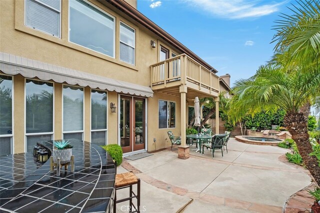 view of patio with outdoor dining area, an in ground hot tub, and a balcony