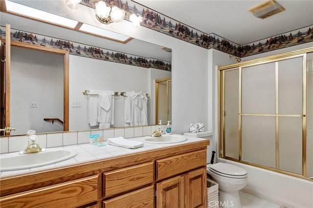 full bath featuring shower / bath combination with glass door, double vanity, toilet, and a sink