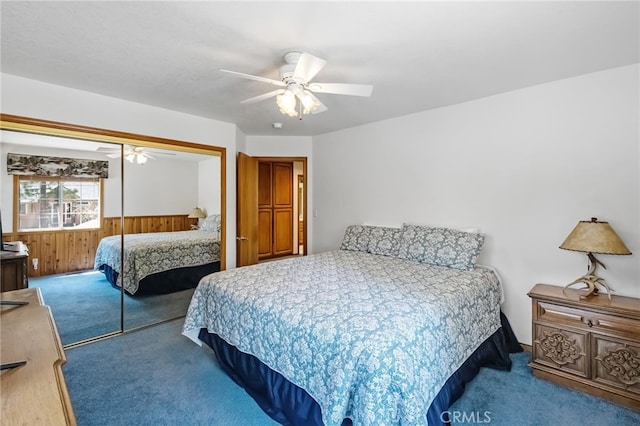 carpeted bedroom featuring wooden walls, a closet, a wainscoted wall, and a ceiling fan