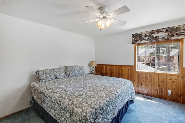 carpeted bedroom with wooden walls, visible vents, a ceiling fan, and wainscoting