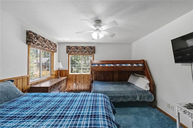 bedroom with carpet flooring, a textured ceiling, wainscoting, wood walls, and ceiling fan