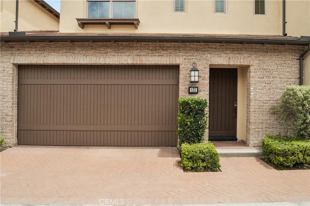 property entrance with a garage, brick siding, and stucco siding