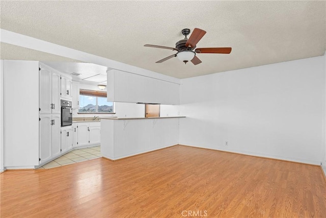 unfurnished living room with light wood-style flooring, a textured ceiling, and a ceiling fan