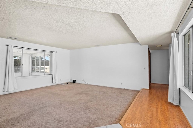 carpeted empty room with wood finished floors, visible vents, and a textured ceiling