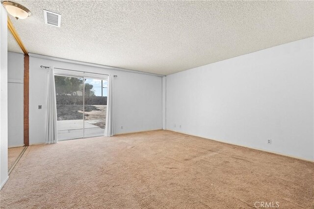 carpeted empty room featuring a textured ceiling and visible vents