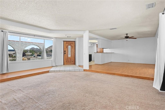 unfurnished living room featuring light colored carpet, ceiling fan, a textured ceiling, and visible vents