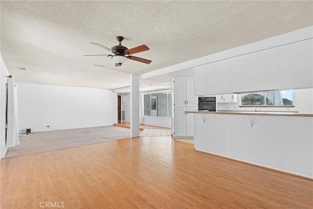 unfurnished living room featuring light wood-type flooring, visible vents, a textured ceiling, and ceiling fan