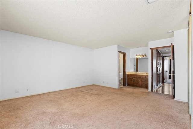 unfurnished bedroom with light colored carpet, ensuite bath, and a textured ceiling