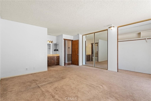 unfurnished bedroom featuring carpet flooring, a textured ceiling, visible vents, two closets, and connected bathroom