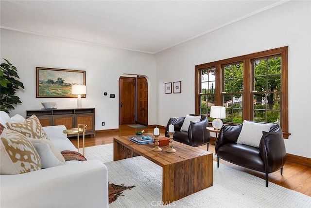 living area featuring baseboards, arched walkways, light wood-style floors, and crown molding