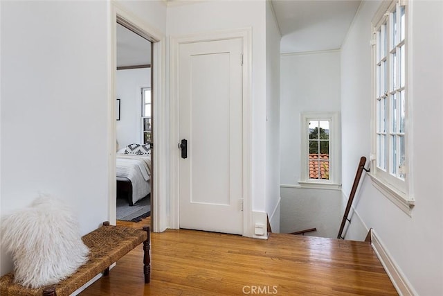 hall with baseboards, wood finished floors, an upstairs landing, and ornamental molding