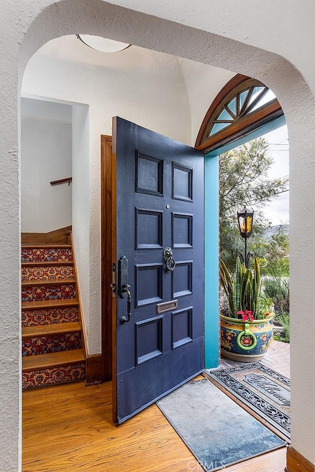 entrance foyer featuring arched walkways, a textured wall, stairs, and wood finished floors