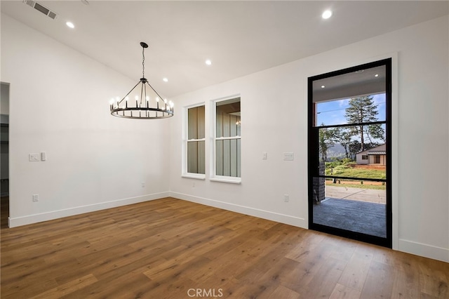 unfurnished dining area featuring a chandelier, visible vents, vaulted ceiling, baseboards, and wood finished floors