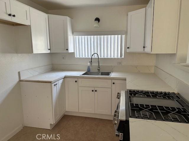 kitchen featuring light stone counters, stainless steel gas range oven, white cabinets, a sink, and light tile patterned flooring