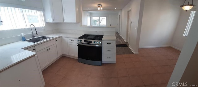 kitchen with white cabinets, light stone counters, stainless steel range with gas stovetop, and a sink
