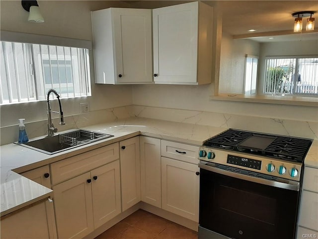 kitchen featuring white cabinetry, stainless steel gas range oven, light stone counters, and a sink