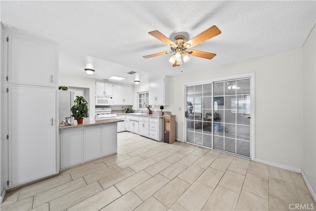 kitchen featuring white cabinets, a peninsula, a textured ceiling, a ceiling fan, and white appliances