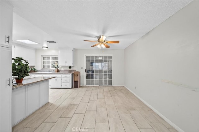 kitchen featuring white cabinets, baseboards, a textured ceiling, and ceiling fan