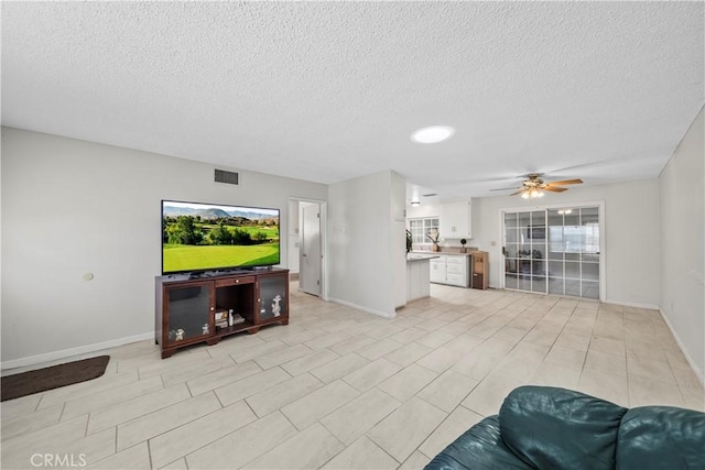 living area featuring a textured ceiling, visible vents, a ceiling fan, and baseboards