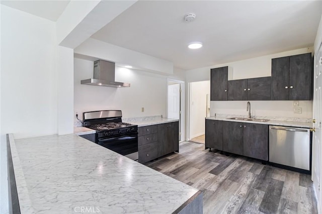 kitchen with stainless steel dishwasher, a peninsula, a sink, black range with gas cooktop, and wall chimney exhaust hood