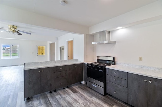 kitchen featuring gas range, wall chimney exhaust hood, wood finished floors, a peninsula, and a ceiling fan