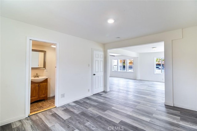 empty room featuring wood finished floors, baseboards, recessed lighting, and a sink