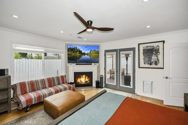 living area with a warm lit fireplace, wood finished floors, visible vents, a ceiling fan, and crown molding