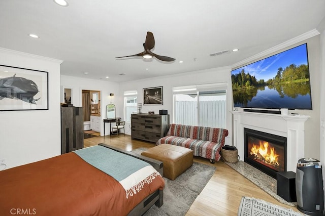 bedroom with wood finished floors, a glass covered fireplace, ornamental molding, visible vents, and recessed lighting