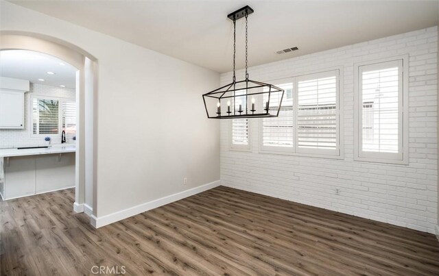 30461 Savoie St, Murrieta, CA 92563 - unfurnished dining area featuring arched walkways, brick wall, baseboards, wood finished floors, and visible vents