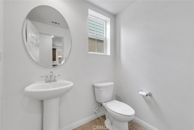 half bath with tile patterned floors, a sink, toilet, baseboards, and visible vents
