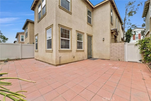 rear view of house with a patio, stucco siding, and fence