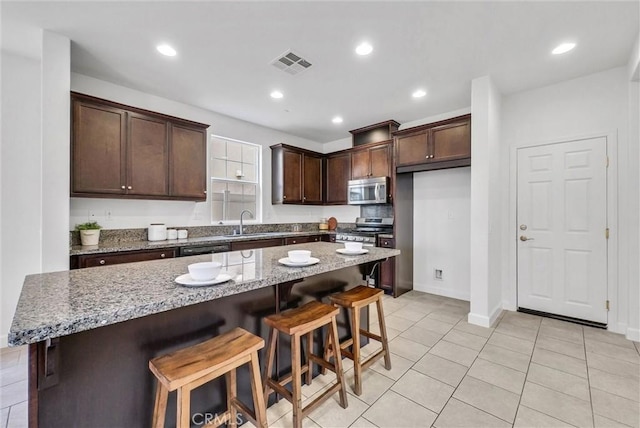 kitchen featuring dark brown cabinets, visible vents, a sink, light tile patterned flooring, and appliances with stainless steel finishes