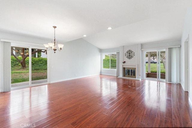 unfurnished living room with baseboards, a brick fireplace, wood finished floors, and a notable chandelier