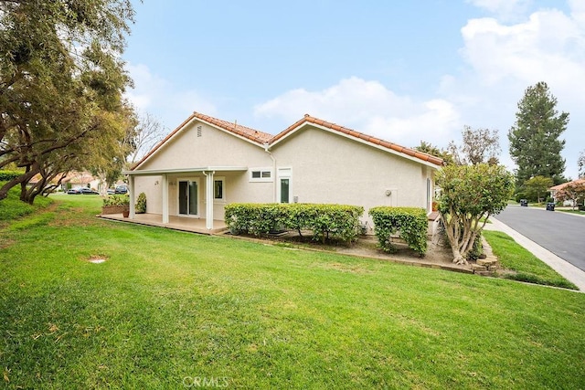 back of property with a lawn, a tiled roof, and stucco siding