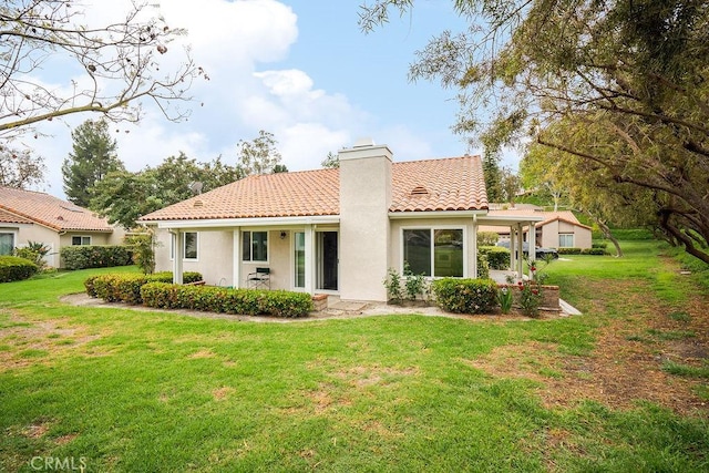 rear view of house featuring a chimney, a yard, a tiled roof, and stucco siding