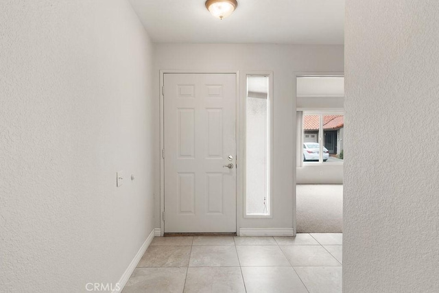 foyer entrance featuring a textured wall, baseboards, and light tile patterned flooring