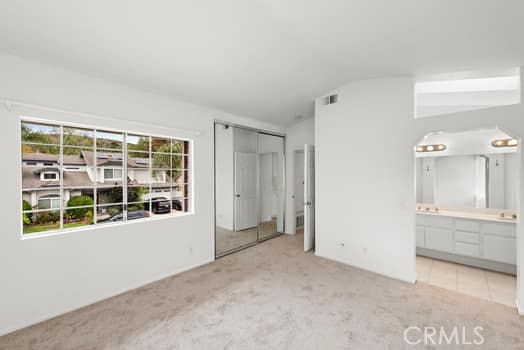 unfurnished bedroom with carpet floors, a closet, visible vents, connected bathroom, and vaulted ceiling