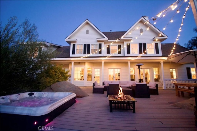 back of house at twilight featuring an outdoor living space with a fire pit, a wooden deck, french doors, and an outdoor hot tub