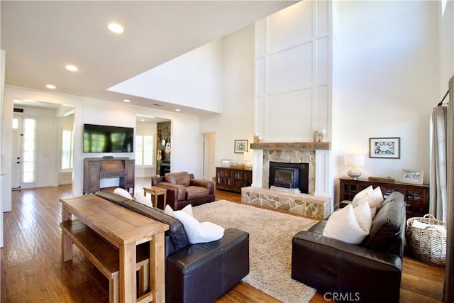 living room featuring hardwood / wood-style flooring, recessed lighting, a towering ceiling, and a fireplace