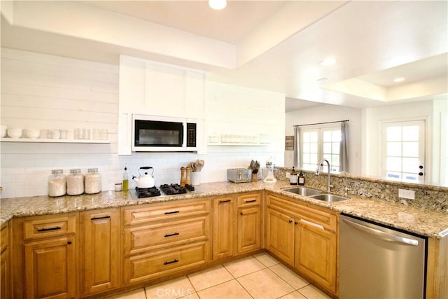 kitchen with light stone counters, stainless steel appliances, a raised ceiling, a sink, and a peninsula