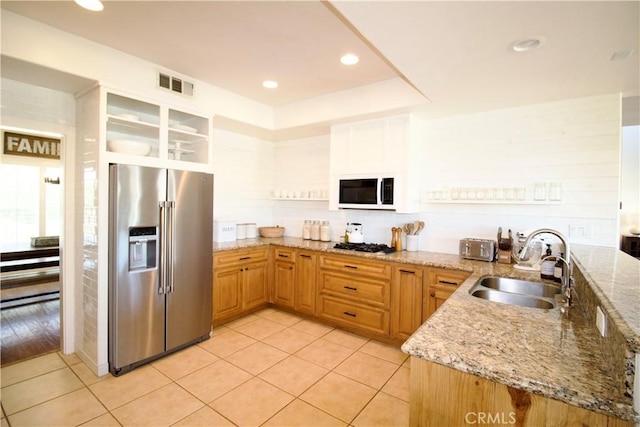 kitchen with a sink, high end refrigerator, visible vents, white microwave, and light stone countertops