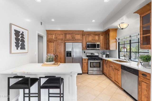 kitchen with stainless steel appliances, a kitchen bar, a sink, and brown cabinets