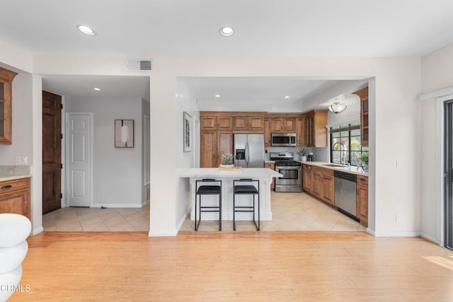 kitchen featuring stainless steel appliances, a sink, visible vents, brown cabinetry, and light countertops