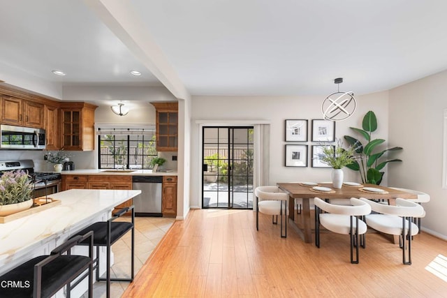 kitchen with brown cabinets, recessed lighting, light wood-style floors, glass insert cabinets, and appliances with stainless steel finishes
