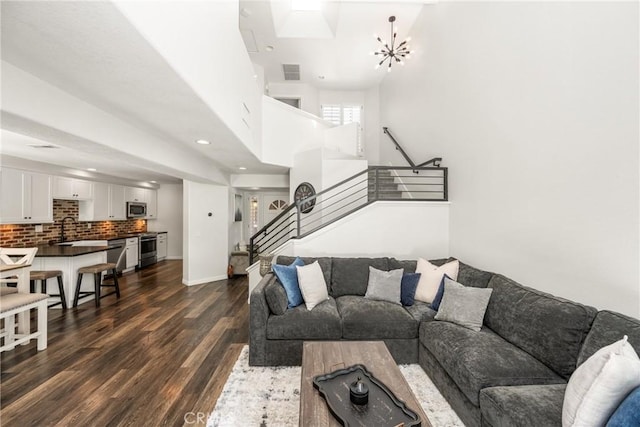 living room with dark wood finished floors, a towering ceiling, visible vents, an inviting chandelier, and stairs