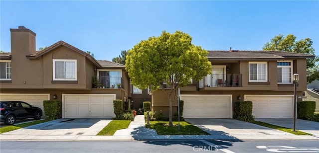 multi unit property featuring an attached garage, driveway, a chimney, and stucco siding